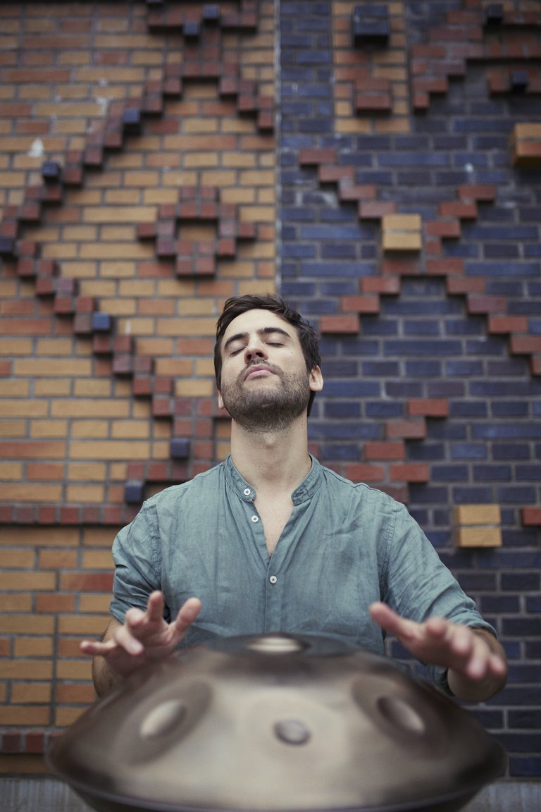 Lorenz Schmidt mit geschlossenen Augen über seiner Handpan, vor einer gemusterten Ziegelwand